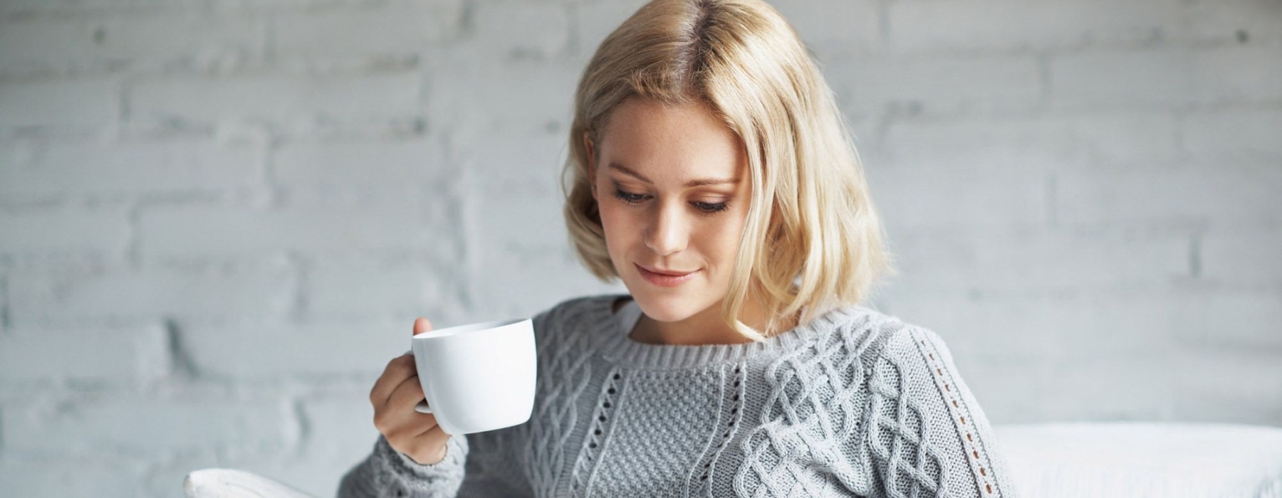 a woman sits on a couch with a cup of coffee and looks at her tablet